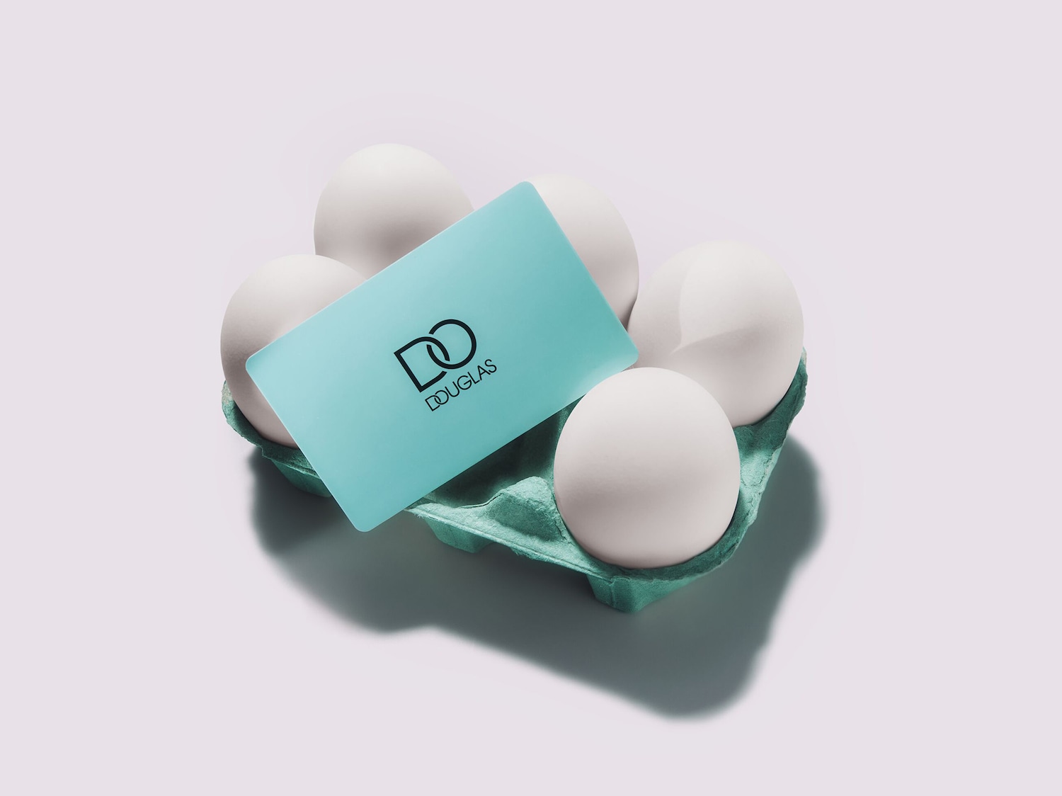 Ein hellblaues Douglas-Geschenkkarte liegt auf einer grünen Eierpalette, umgeben von fünf weißen Eiern.