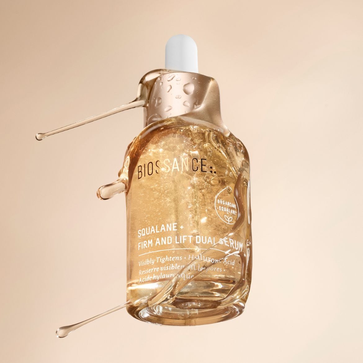 Close-up of Biossance Squalane Firm and Lift Dual Serum in a clear bottle with a white dropper, featuring golden liquid and the text 'Visibly Tightens' for promoting skin firmness.