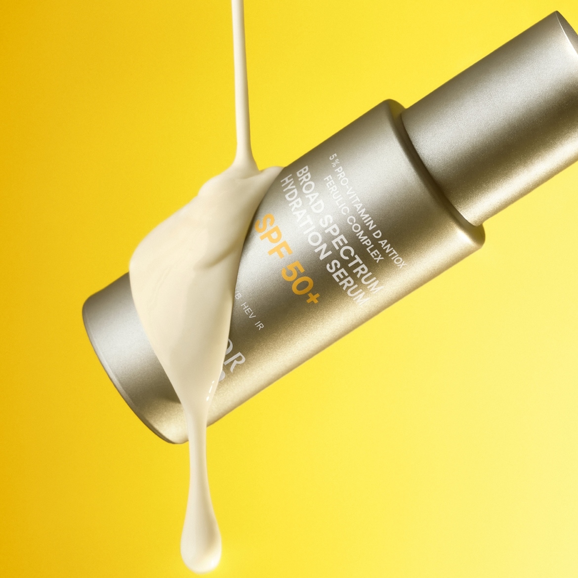Auf gelbem Hintergrund ist eine Tube Sonnenserum mit SPF 50+ zu sehen, auf die eine cremefarbene Flüssigkeit gegossen wird, die die feuchtigkeitsspendende und schützende Wirkung des Produkts hervorhebt.