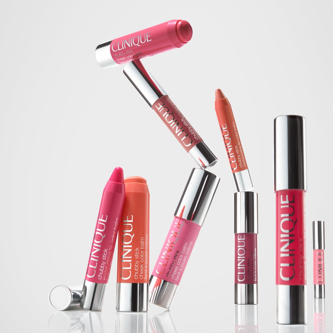 Eine Sammlung von Clinique Chubby Sticks in verschiedenen Farben, darunter Rosa-, Korallen- und Rottöne, sowohl für Lippen als auch für Wangen, die auf einem glänzenden, reflektierenden Untergrund angeordnet sind.