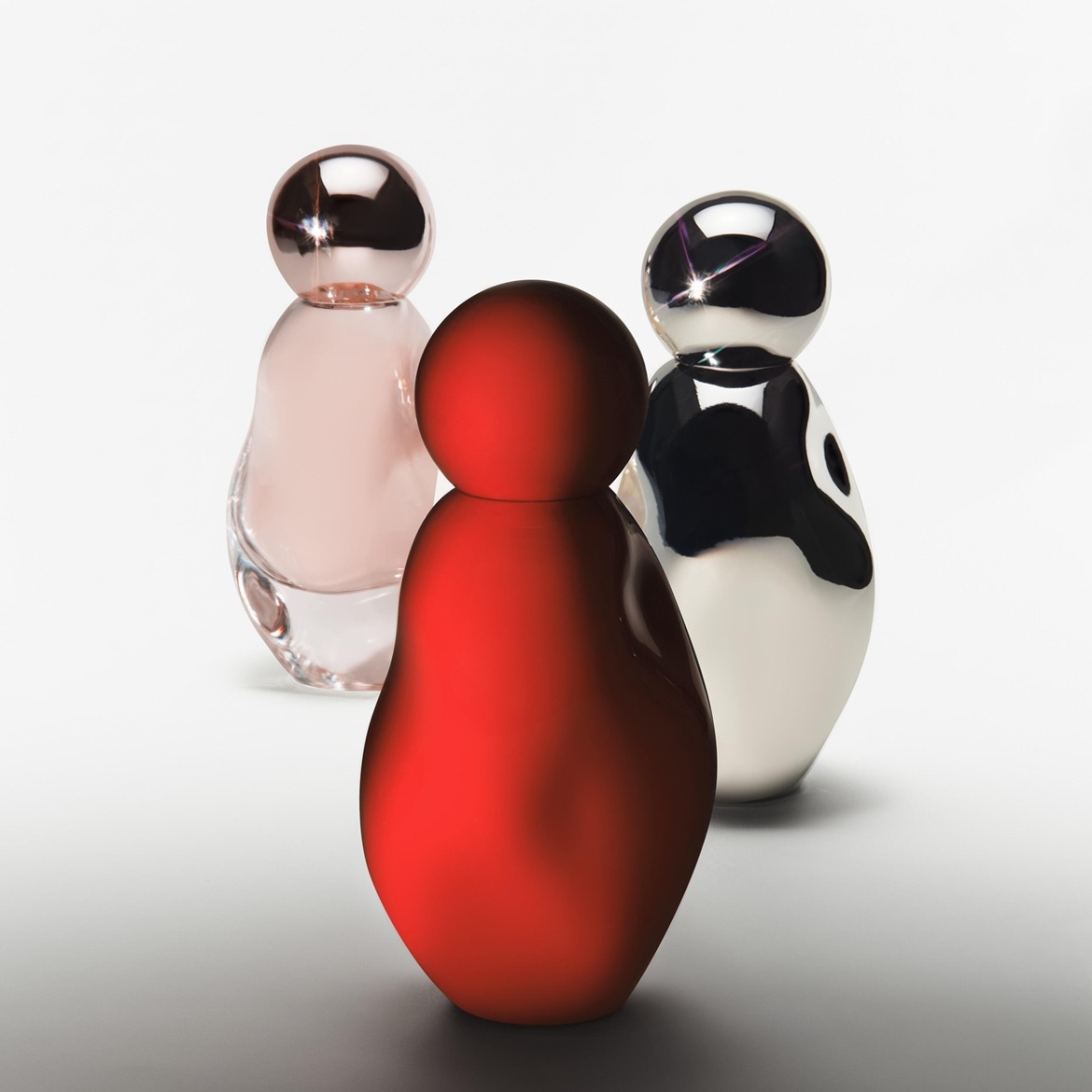 Drei Flakons in Rot, Rosa und Schwarz-Weiß stehen auf einem hellen Untergrund und bilden eine moderne, skulpturale Anordnung.