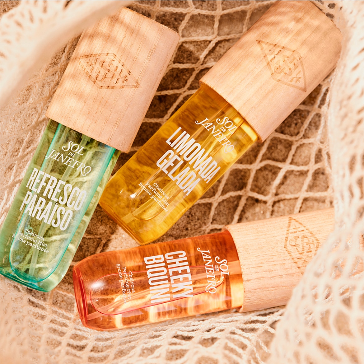 Three Sol de Janeiro perfume mists in green, yellow, and orange bottles with wooden caps, each labeled with a unique scent name.