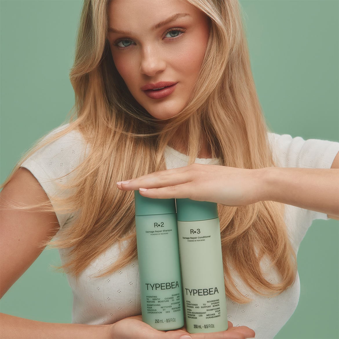 Eine blonde Frau hält zwei mintgrüne Flaschen von Typebea in den Händen, R.2 Damage Repair Shampoo und R.3 Damage Repair Conditioner, die jeweils 250 ml Inhalt haben.
