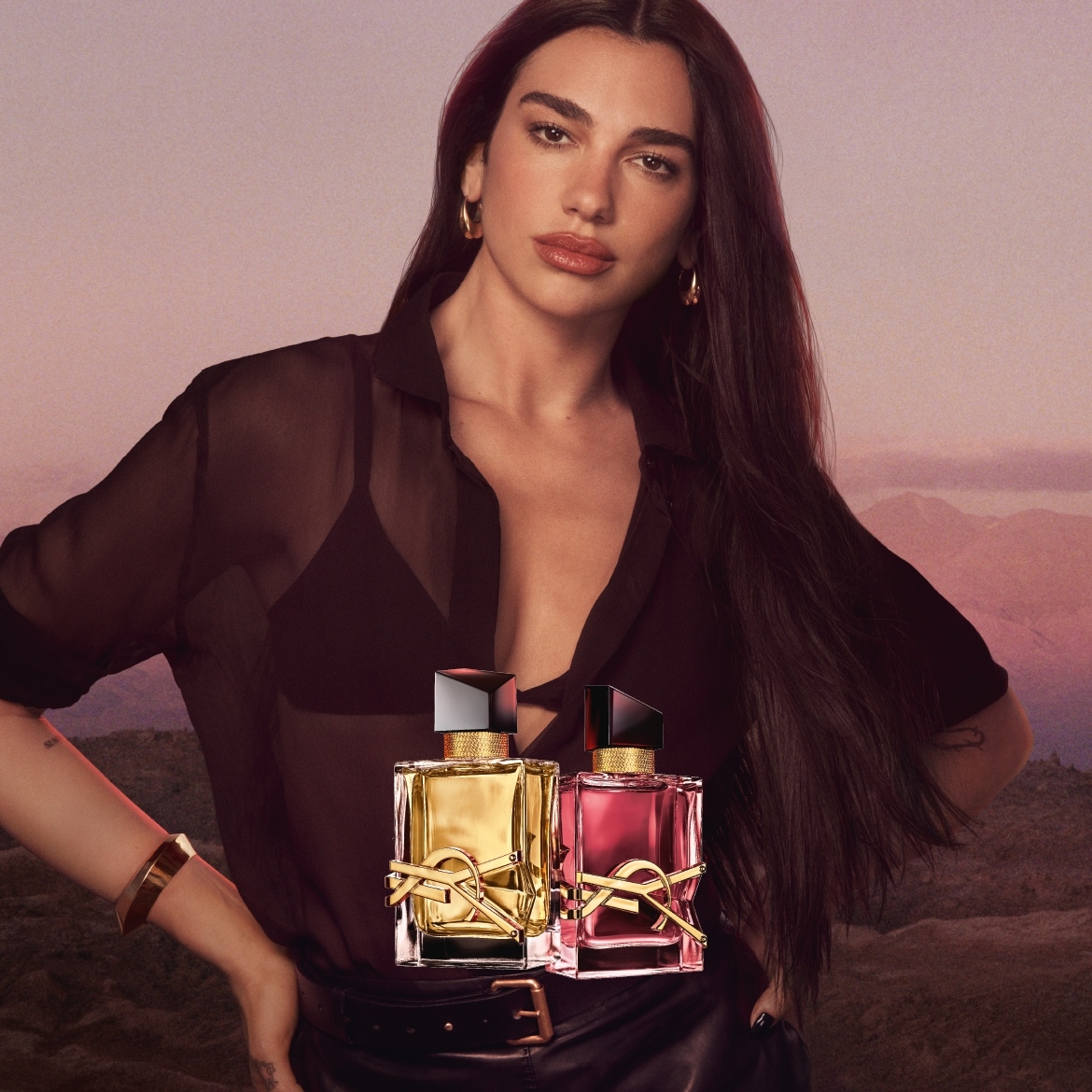Dua Lipa präsentiert zwei Flakons von Yves Saint Laurent: Einer in Gold und einer in Pink, beide mit dem ikonischen YSL-Logo.