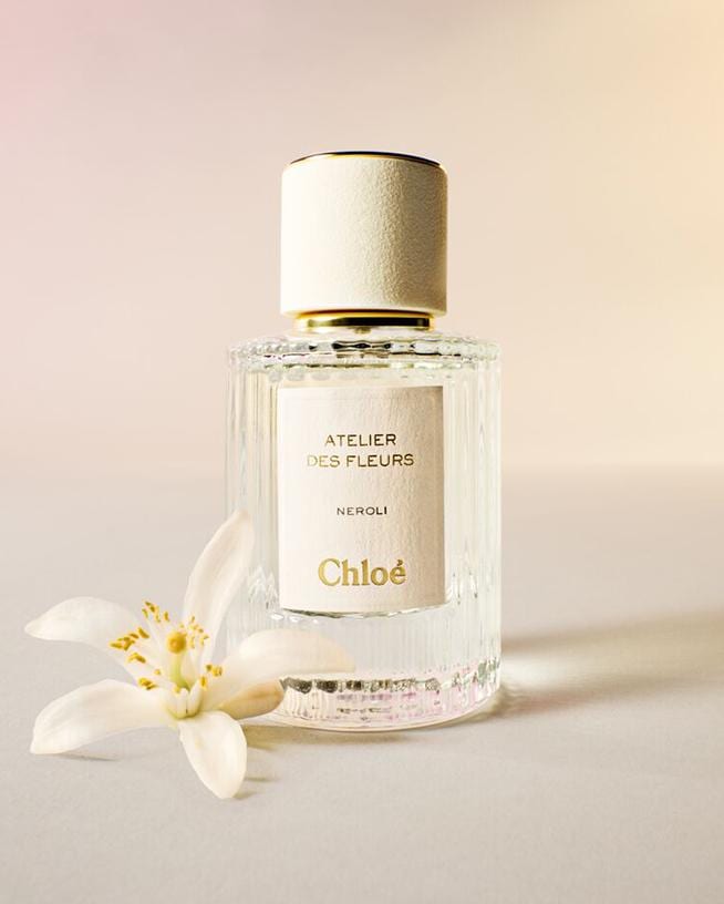 Chloé Atelier des Fleurs Neroli Duft in einem durchsichtigen Glasflakon mit weißem Etikett und Verschluss, daneben eine Neroli-Blüte.