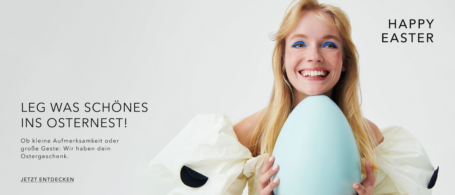 Happy Easter! A blonde woman in a white dress with black polka dots smiles, holding a giant, light blue Easter egg, with text that says: Put something nice in your Easter nest! Discover your Easter gift now.
