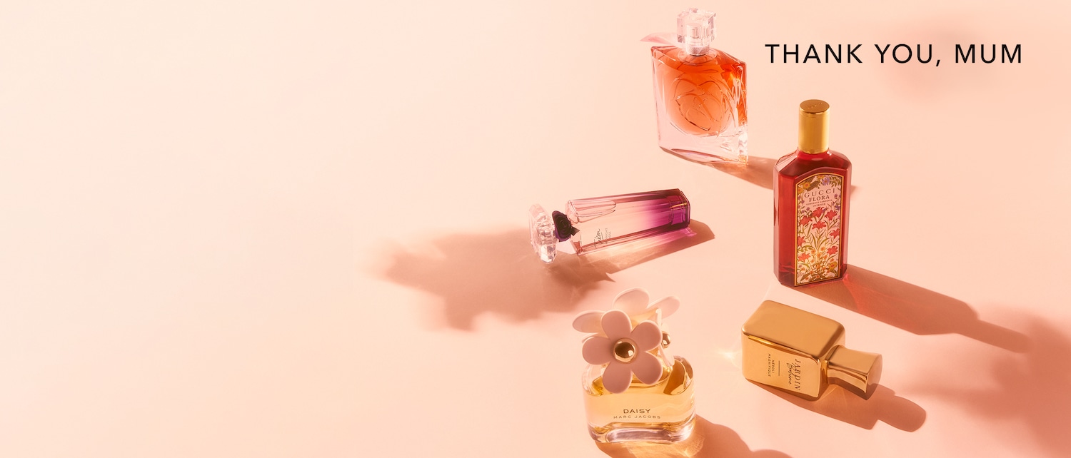 Verschiedene Parfums der Marken Marc Jacobs, Gucci und Lancôme sind auf einem rosafarbenen Hintergrund angeordnet, um "Danke, Mama" zu sagen.