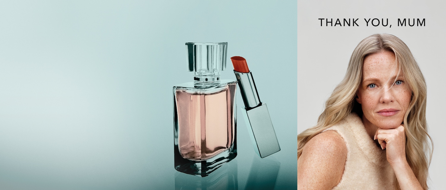 Ein elegantes Stillleben zeigt einen Parfümflakon mit rosa Flüssigkeit und einen silbernen Lippenstift mit roter Spitze, daneben das Porträt einer Frau mit blonden Haaren und blauen Augen, darüber der Schriftzug „DANKE, MAMA“.