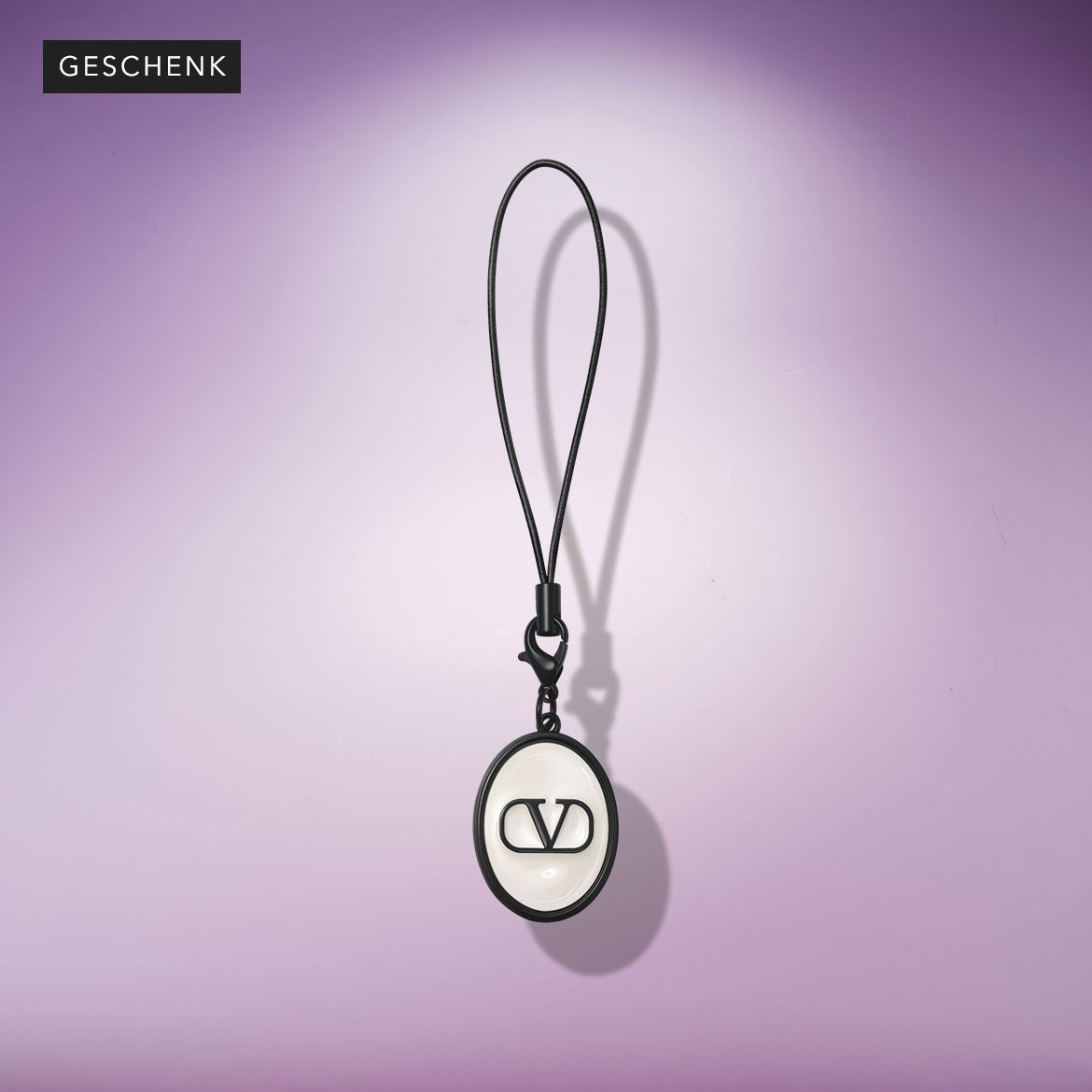 Schwarzer Schlüsselanhänger mit dem Valentino-Logo an einem schwarzen Band, das an einem Karabinerhaken befestigt ist, vor einem violetten Hintergrund.