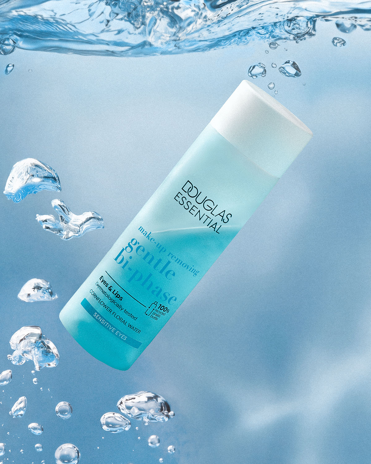 Die Douglas Essential sanfte 2-Phasen-Make-up-Entfernerflasche für Augen und Lippen, dermatologisch getestet mit Kornblumenblütenwasser für empfindliche Augen, schwebt in blauem Wasser mit Blasen.