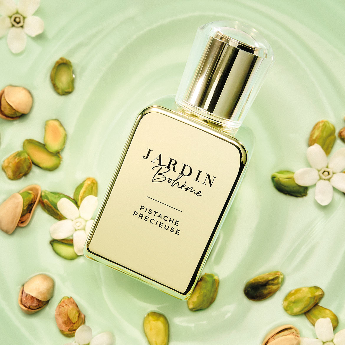 Der Duft „Pistache Précieuse“ von JARDIN Bohème in einem eleganten, rechteckigen Flakon mit goldener Kappe, umgeben von Pistazien und weißen Blüten auf einem hellgrünen Hintergrund.