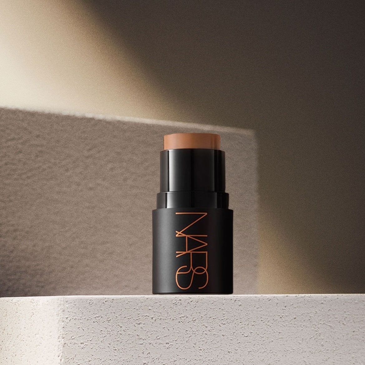 Der NARS Foundation Stick in einem eleganten schwarzen Gehäuse mit orangefarbenem Logo, der auf einer hellen Oberfläche steht, bietet eine makellose Abdeckung für einen strahlenden Teint.