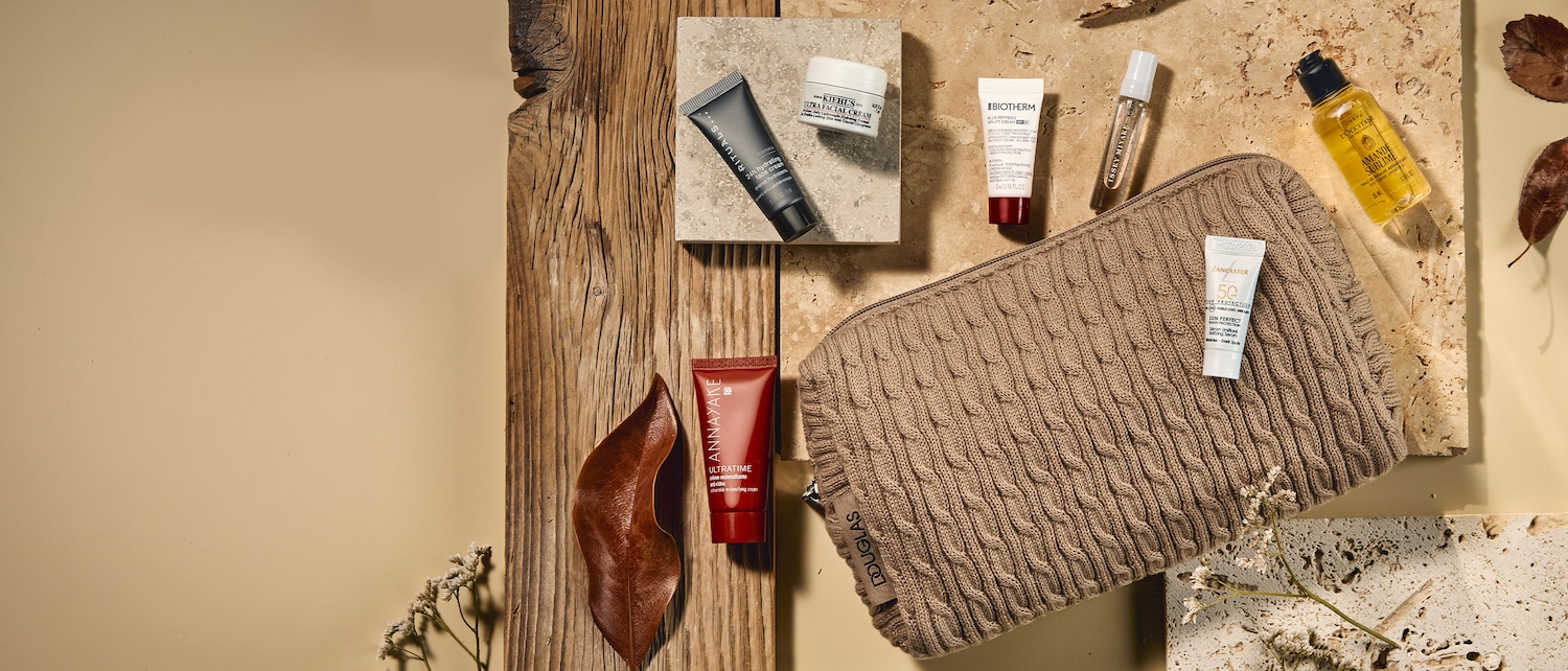 Eine Auswahl an Hautpflegeprodukten, darunter eine schwarze Tube Rituals 24h Feuchtigkeitscreme, ein weißer Tiegel Kiehl's Ultra Facial Cream und eine rote Tube Annayake Ultratime Creme, ist auf beigen und braunen Holzoberflächen angeordnet.