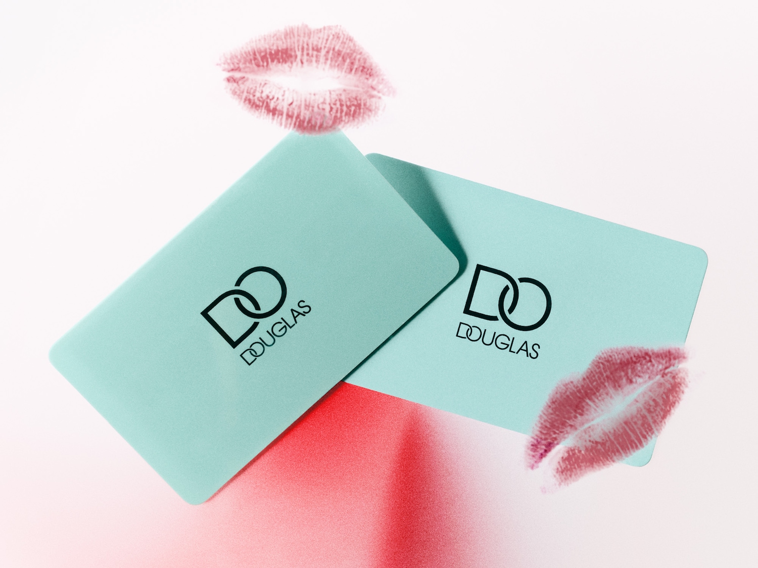 Zwei hellblaue Douglas-Geschenkkarten liegen übereinander, verziert mit roten Kussmund-Abdrücken, die eine liebevolle Geste für Beauty-Liebhaber symbolisieren.